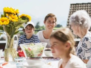 Familie mit Grosseltern essen gemeinsam draussen in der Sonne.